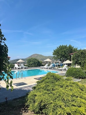 Ein Schwimmbecken mit Liegestühlen, umgeben von Grünpflanzen und einem Berg im Hintergrund.