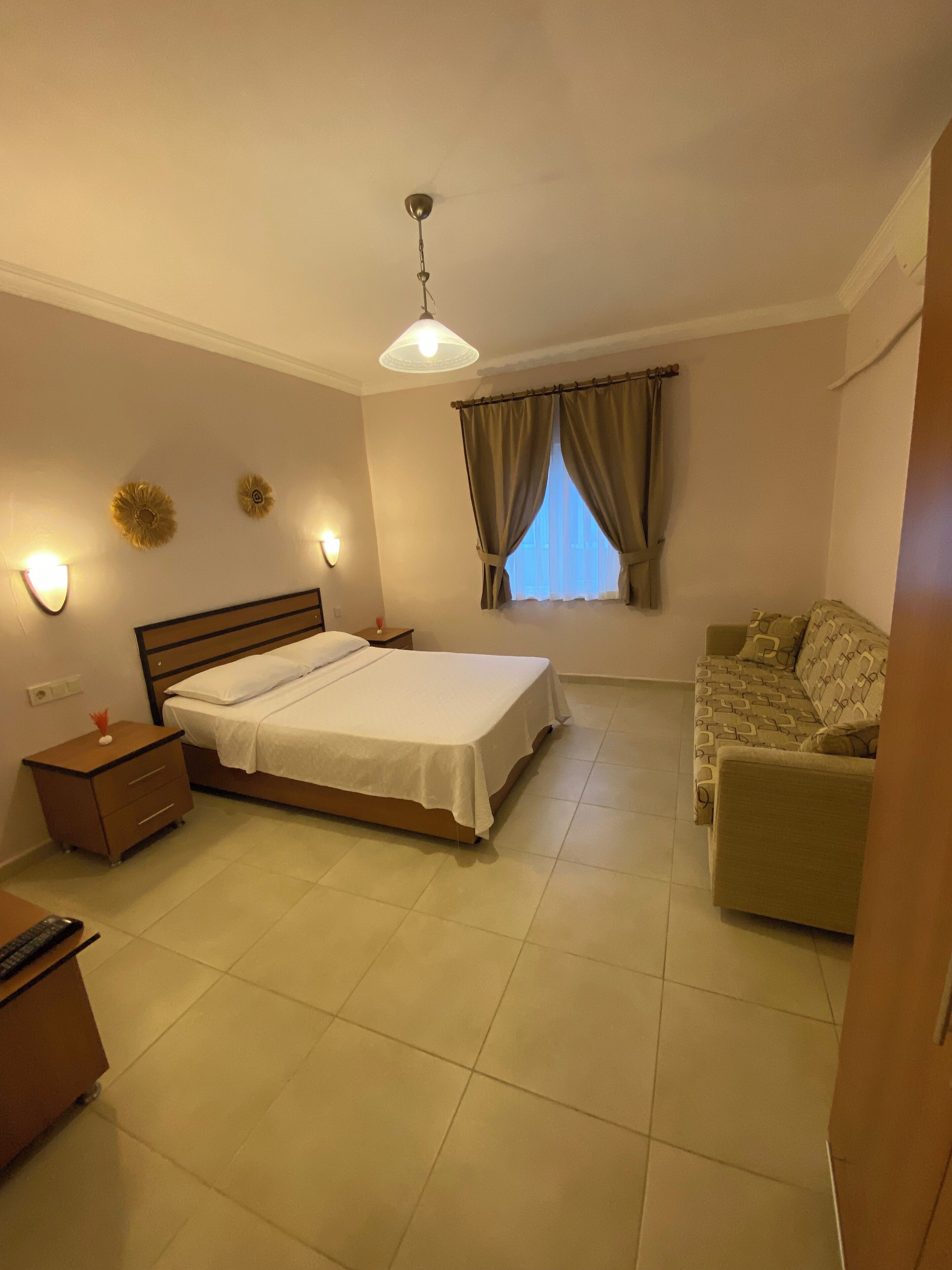 A bedroom with a bed, a nightstand, a sofa, a ceiling fan, and a window with curtains.