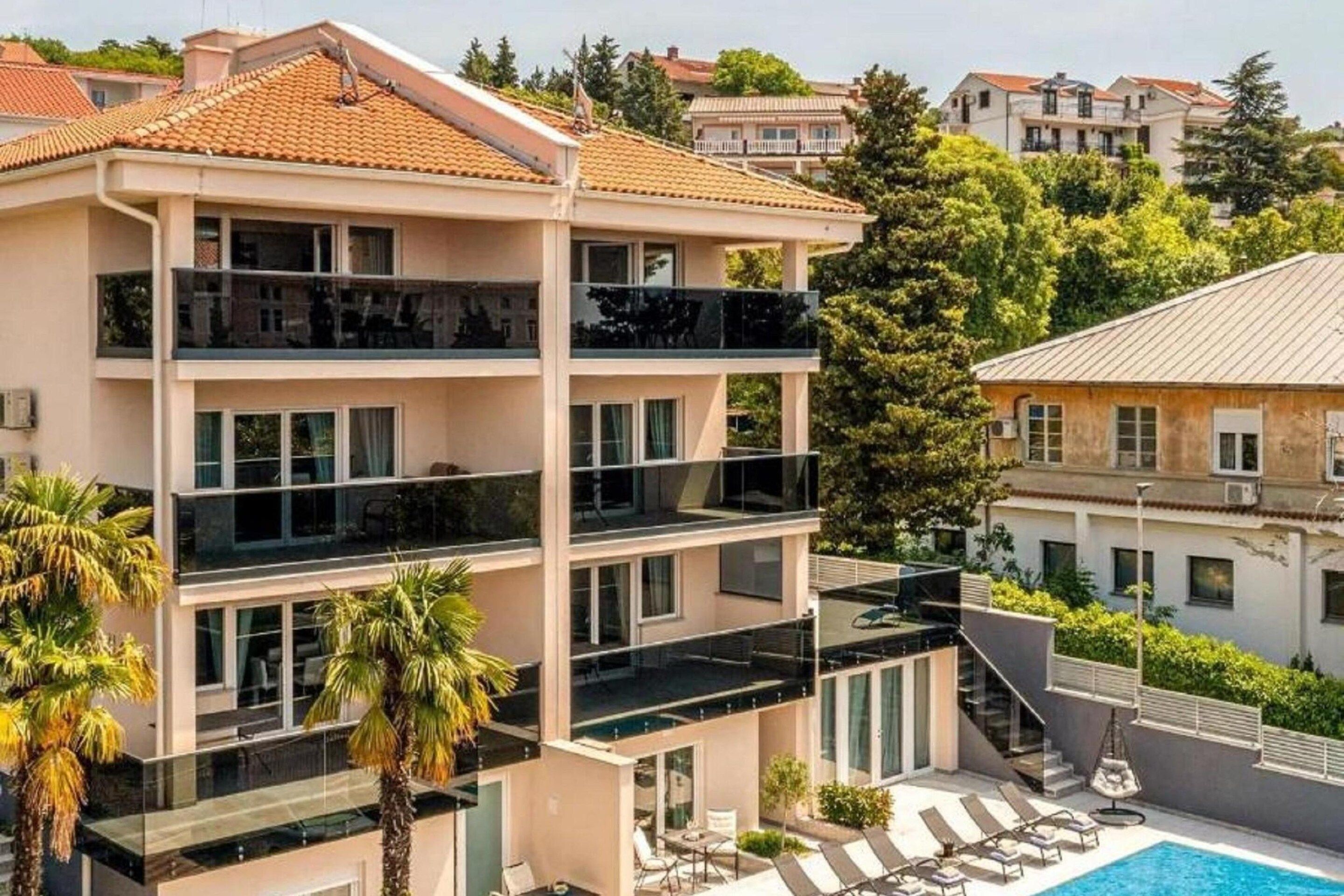 A multi-story building with balconies, a swimming pool, and surrounding greenery.