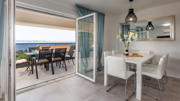 Un balcone con tavolo e sedie, una porta scorrevole in vetro e vista sul mare.