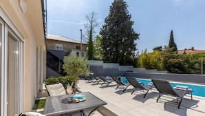 Una terrazza panoramica con piscina, poltrone relax e un tavolo con un drink.