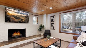 A living room with a fireplace, a large window, a sofa, and a coffee table. - Walk Into The National Park/View (Sevierville)
