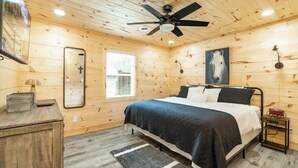 A wooden-paneled bedroom with a bed, a ceiling fan, a mirror, a window, and a nightstand.