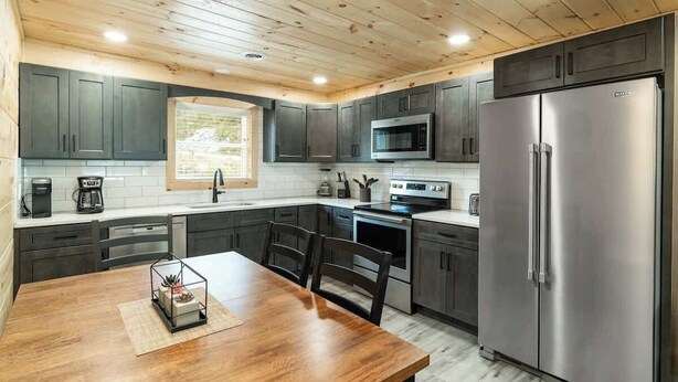 A modern kitchen with dark cabinets, stainless steel appliances, and a wooden dining table.