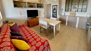 A compact living space with a sofa, a television, a dining table, and a kitchenette. - Casa Raffa by Wonderful Italy (Olbia)
