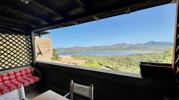 A balcony with a wooden table and chairs, overlooking a scenic landscape with a body of water and hills. - Casa Raffa by Wonderful Italy (Olbia)