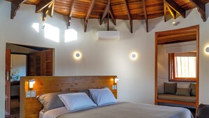 Een slaapkamer met een houten hoofdbord, een bed met grijze beddengoed, een ingebouwde bank met kussens en een plafondventilator.