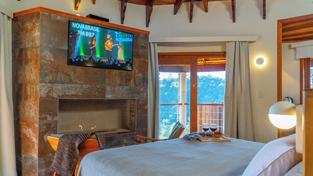 Een hotelkamer met een stenen openhaard, een bed met witte lakens, een aan de muur bevestigde televisie en een balkon met uitzicht op de bergen.