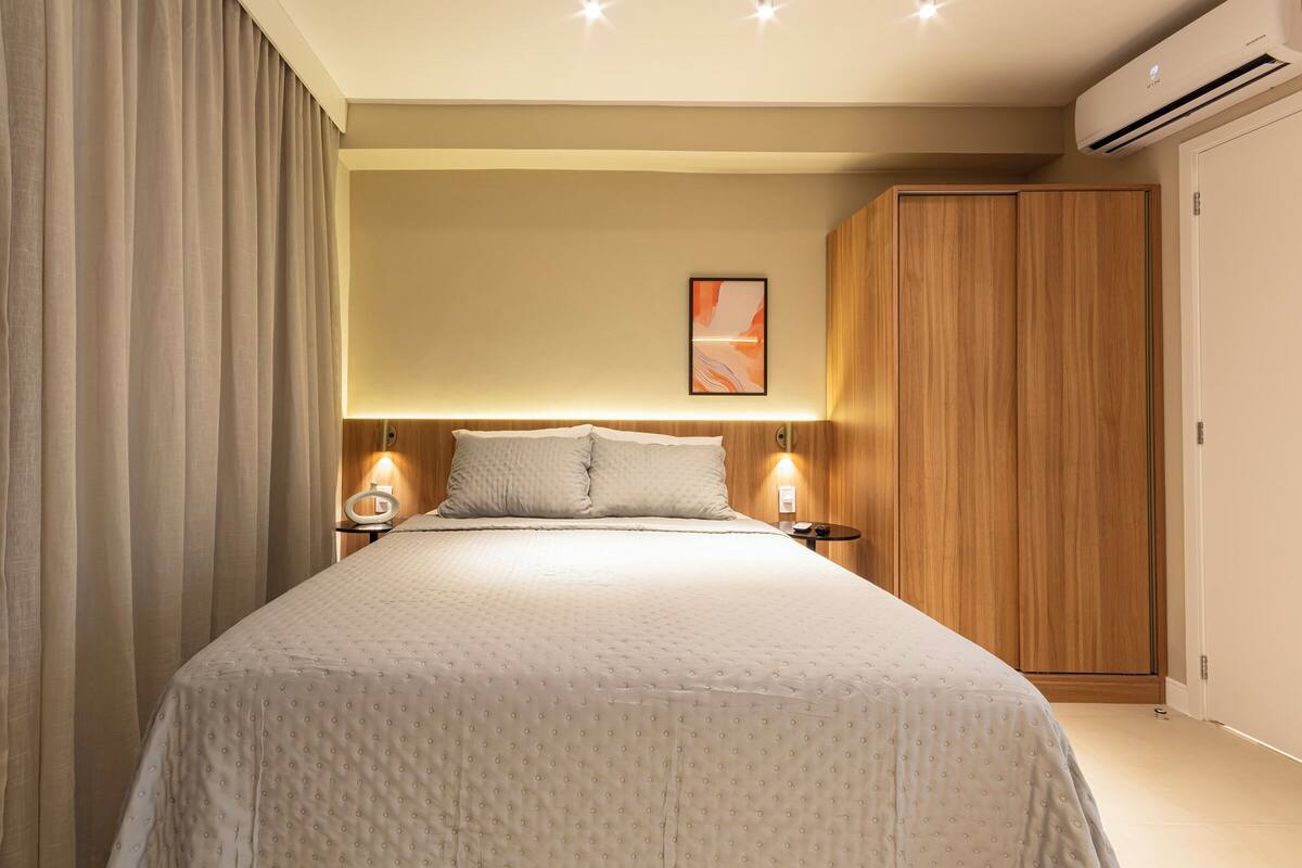 A neatly arranged bedroom with a large bed, two bedside tables, a wooden wardrobe, and an air conditioning unit.