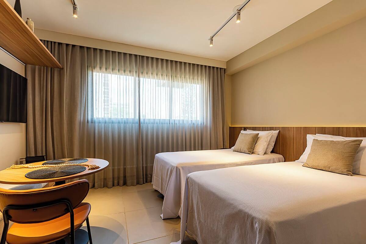 A hotel room with two beds, a desk with a chair, and a large window with curtains.