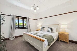 Une chambre bien rangée, avec un lit, des tables de chevet, une fenêtre avec des rideaux, un luminaire suspendu et une vue sur la verdure à l’extérieur.