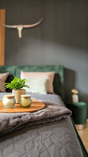 Un lit bien fait, avec une tête de lit verte, une petite plante en pot et deux bocaux posés sur un plateau en bois.