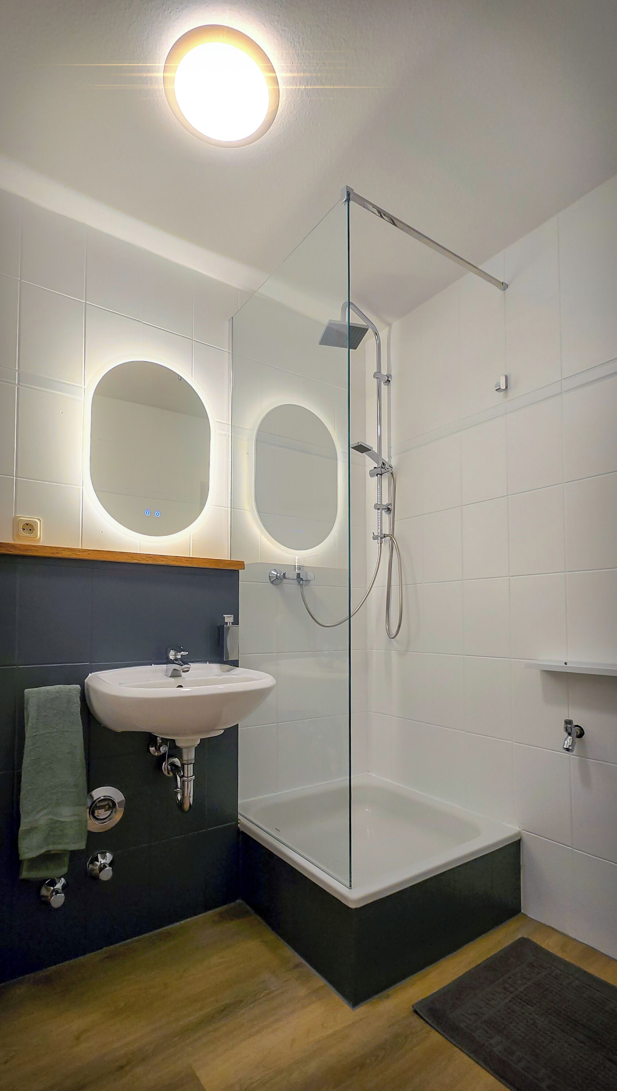 Un baño moderno con ducha envuelta en vidrio, lavamanos pedestal y dos espejos redondos.