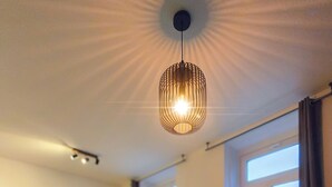 En moderne stue med et centralt kaffebord, en hængende lampe, et fladskærms-tv og udsigt til det fri gennem store vinduer.