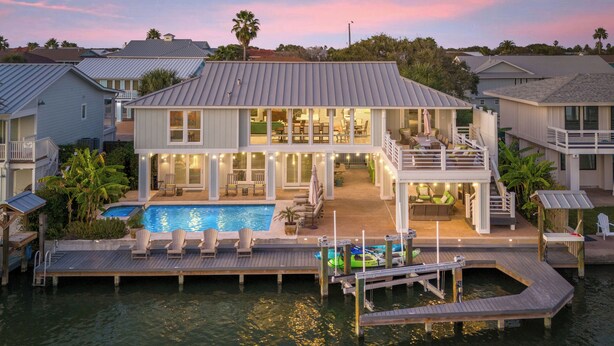 Uma casa à beira-mar com piscina, área de estar externa e um píer.