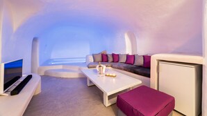 A modern, minimalist interior with a white sofa, a coffee table, and a television. - Kampanario Luxury Villa (Thira - Santorini)
