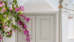 A white door with a keyhole, a potted plant with pink flowers, and a wooden easel in the foreground. - Kampanario Luxury Villa (Thira - Santorini)