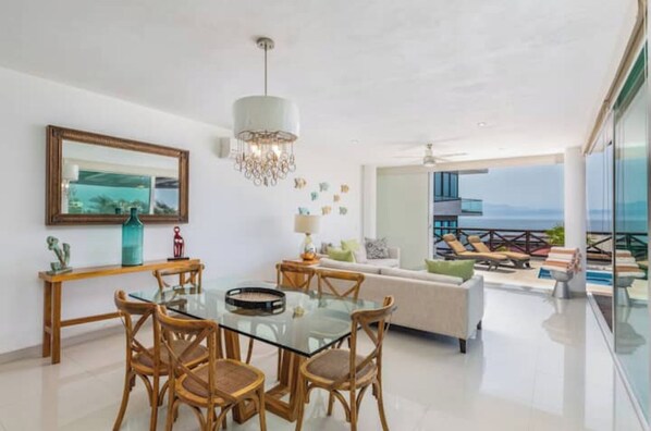 Relax in this stylish living area with a glass dining table and wicker chairs, connected to a balcony with ocean views.