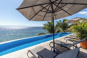 Relax by the oceanfront pool, surrounded by lounge chairs and umbrellas.