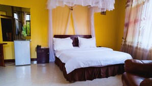 A bedroom with a bed, a nightstand, a dresser, and a refrigerator. - Lenny Hotel Ltd. (Geita)