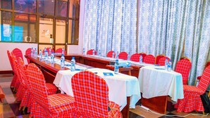A conference room with red checkered chairs, white tables, and a large window with curtains. - Lenny Hotel Ltd. (Geita)