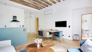 Una sala de estar moderna con comedor, vigas de madera en el techo, un televisor de pantalla plana y un sofá azul.
