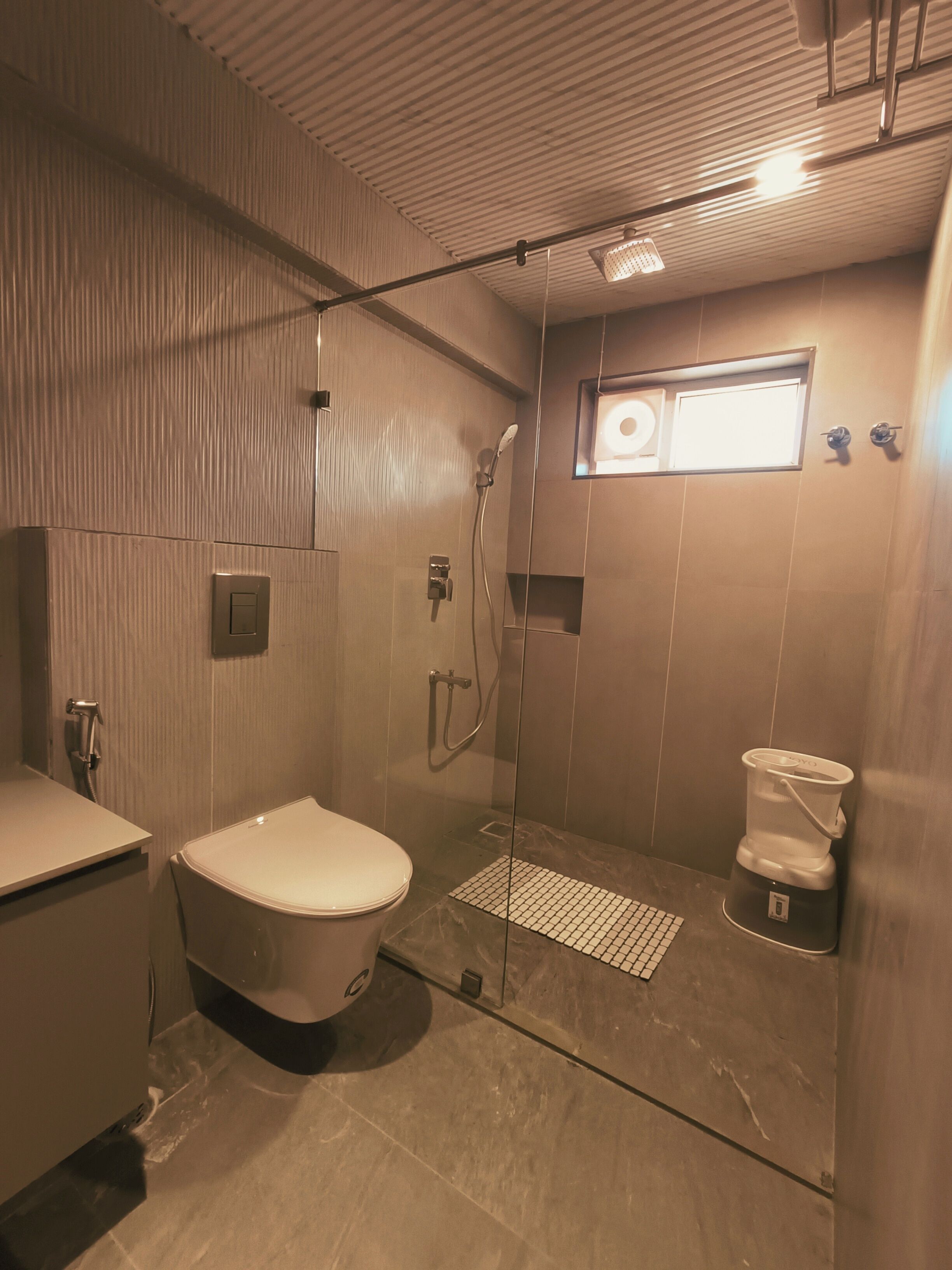 Een moderne badkamer met toilet, douche en een koffiezetapparaat op een plank.
