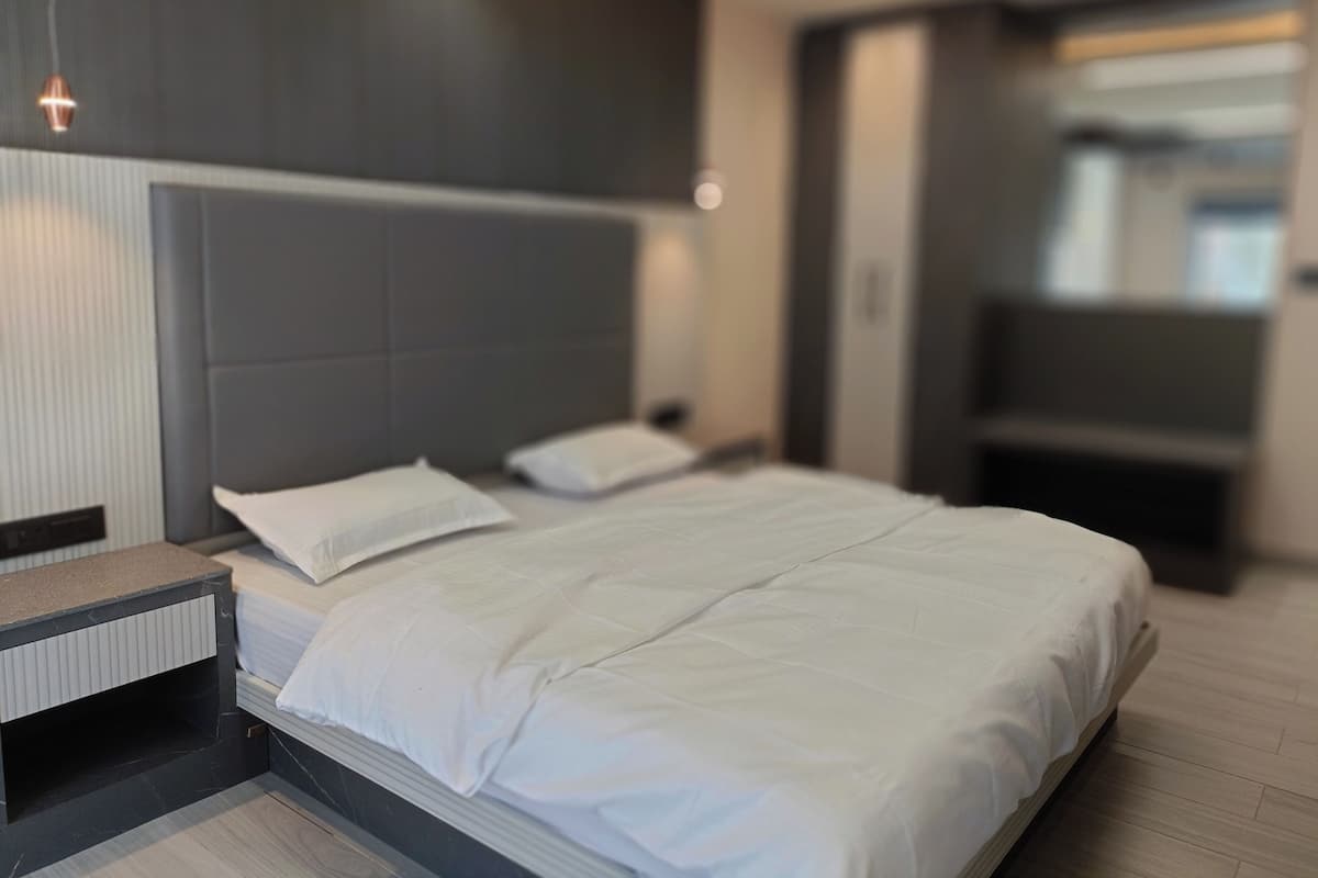 Ein modernes Hotelzimmer mit einem großen Bett, einem Nachttisch und einem integrierten Fernseher.