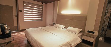 A modern hotel room with a large bed, bedside tables, a coffee maker, and a window with blinds.