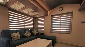 A modern living room with a sectional sofa, a coffee table, and large windows with blinds. - Villa Euphoria (Ootacamund)