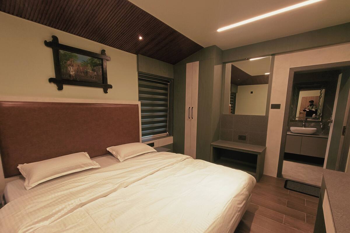 Ein Schlafzimmer mit einem großen Bett, einem Nachttisch, einem Kleiderschrank und einem Badezimmer mit Waschbecken und Spiegel.