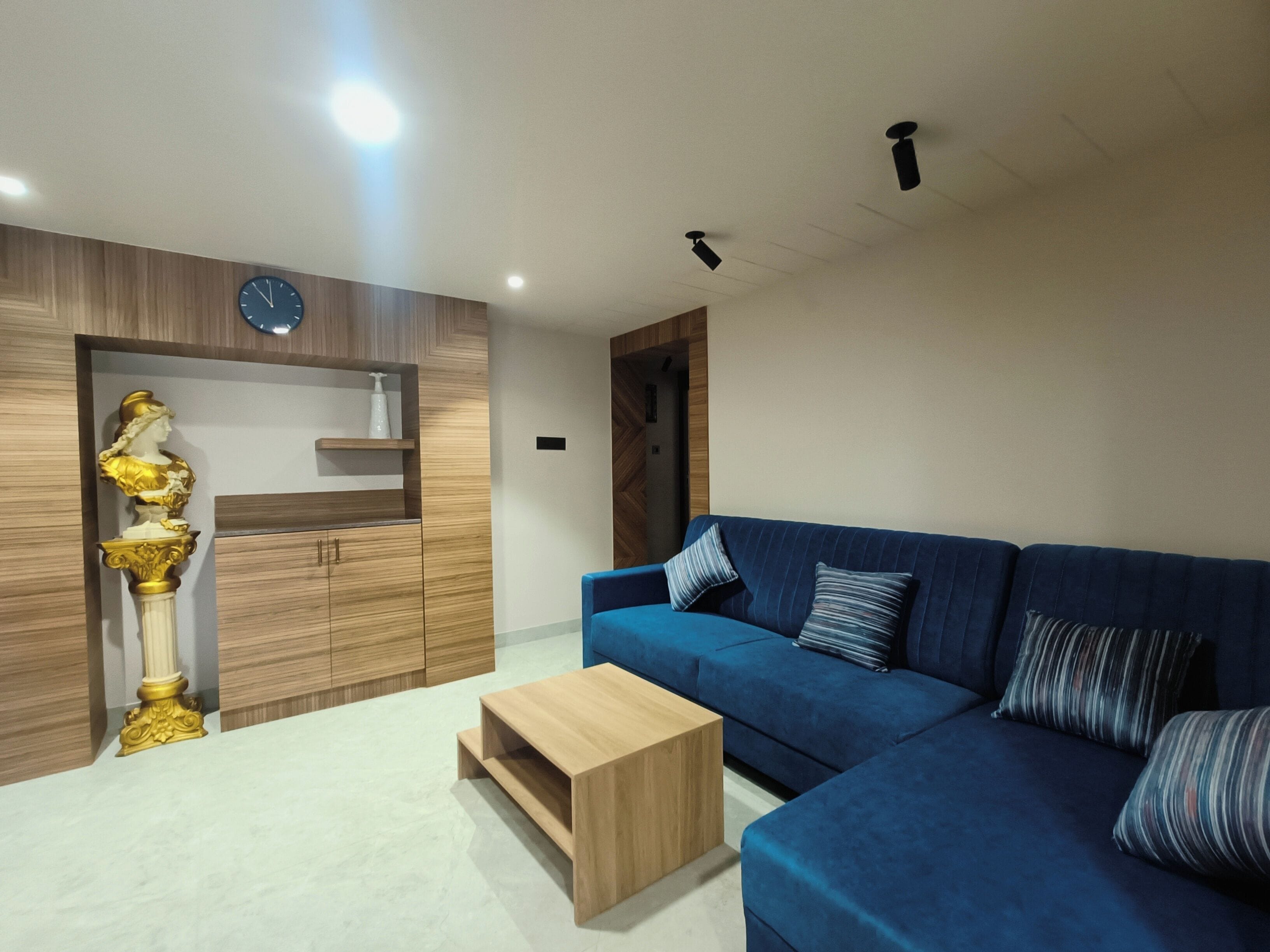 A modern living room with a blue sofa, a wooden coffee table, and a decorative bust on a wooden cabinet.