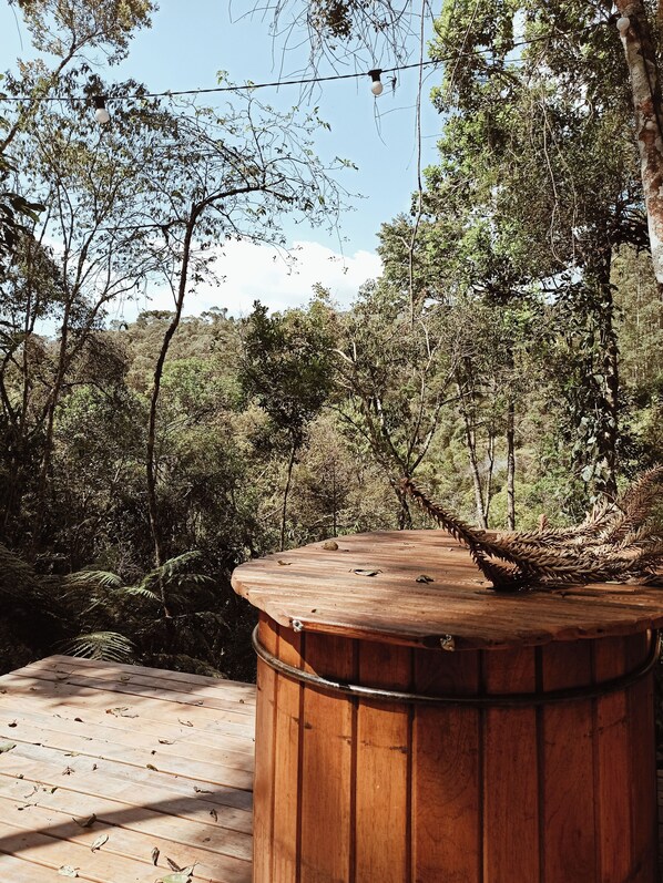 Un bain à remous en bois, entouré d’une forêt dense, sous un ciel dégagé.