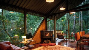 A cozy cabin with a fireplace, comfortable seating, and large windows offering a forest view. - Chale de Vidro nas montanhas (Itamonte)