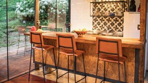 A modern kitchen with a bar area, wooden flooring, and a view of greenery outside. - Chale de Vidro nas montanhas (Itamonte)