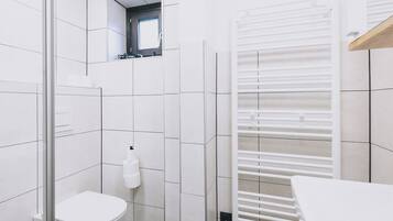 Une salle de bain moderne avec des carreaux blancs, des toilettes, une douche en verre et un porte-serviettes blanc.
