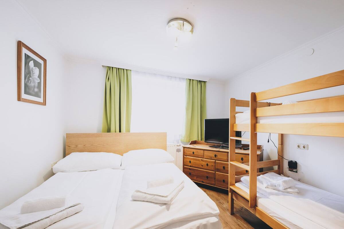 A room with a bed, a TV, a dresser, and a bunk bed.