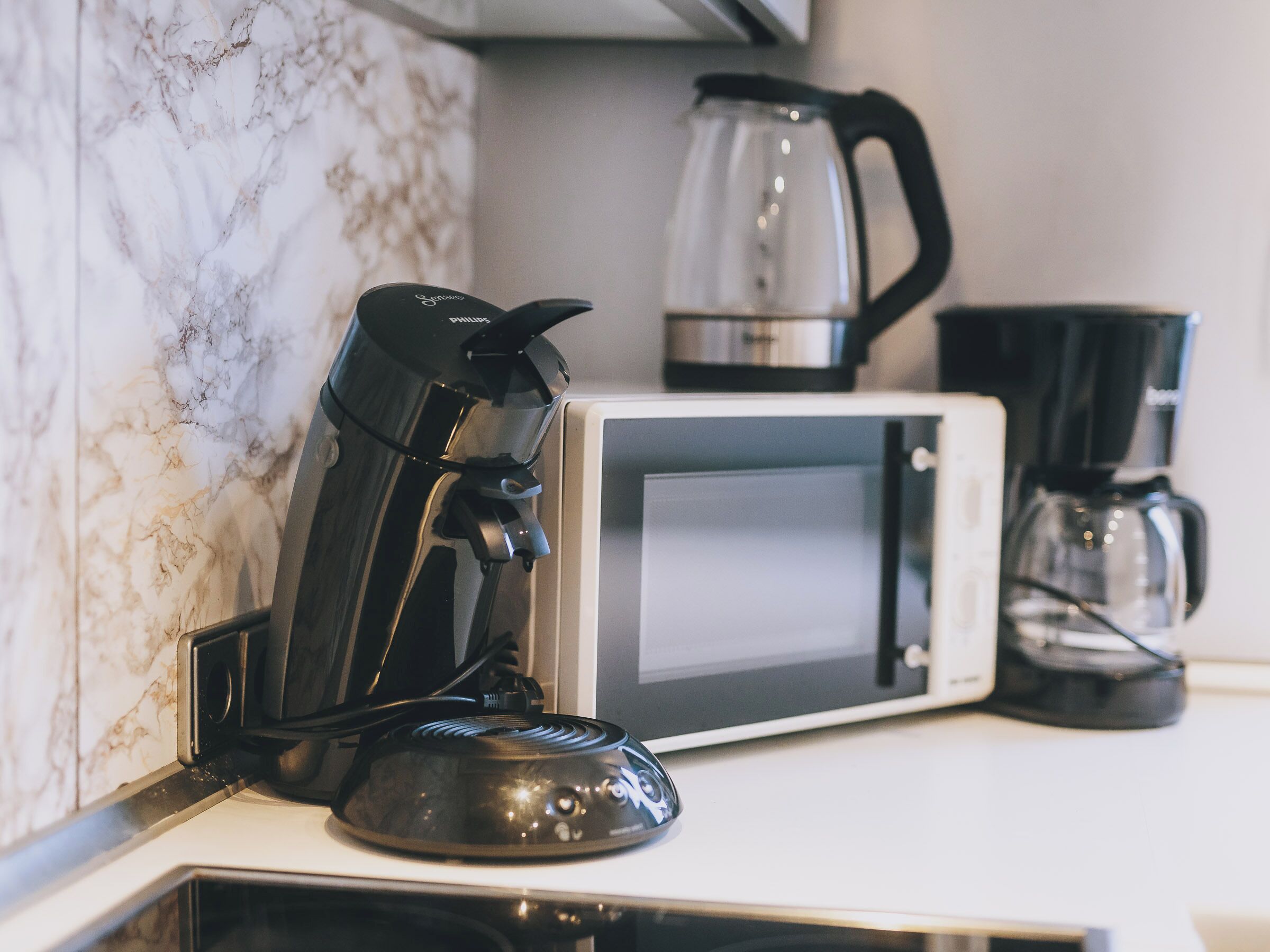 A kitchen with a coffee maker, a microwave, and a kettle.