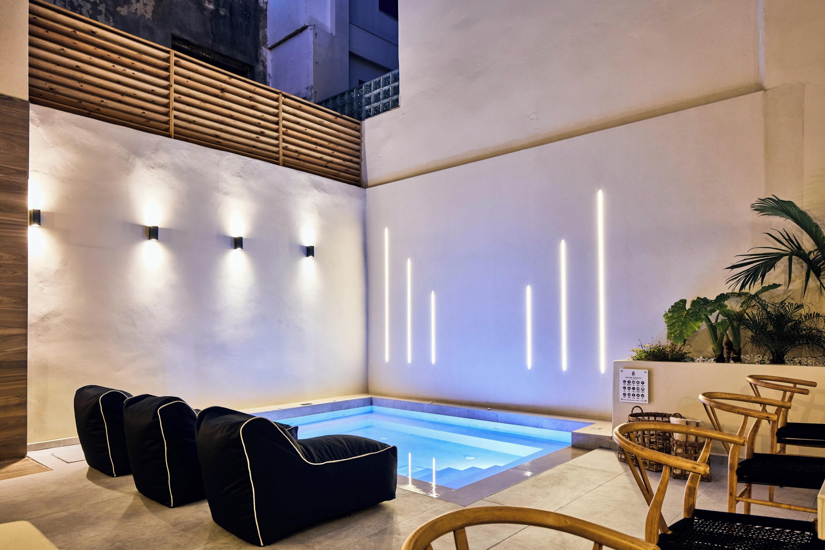 Un espace piscine intérieur moderne, doté d’un coin salon, d’un plafond à lambris en bois et d’un luminaire fixé au mur.
