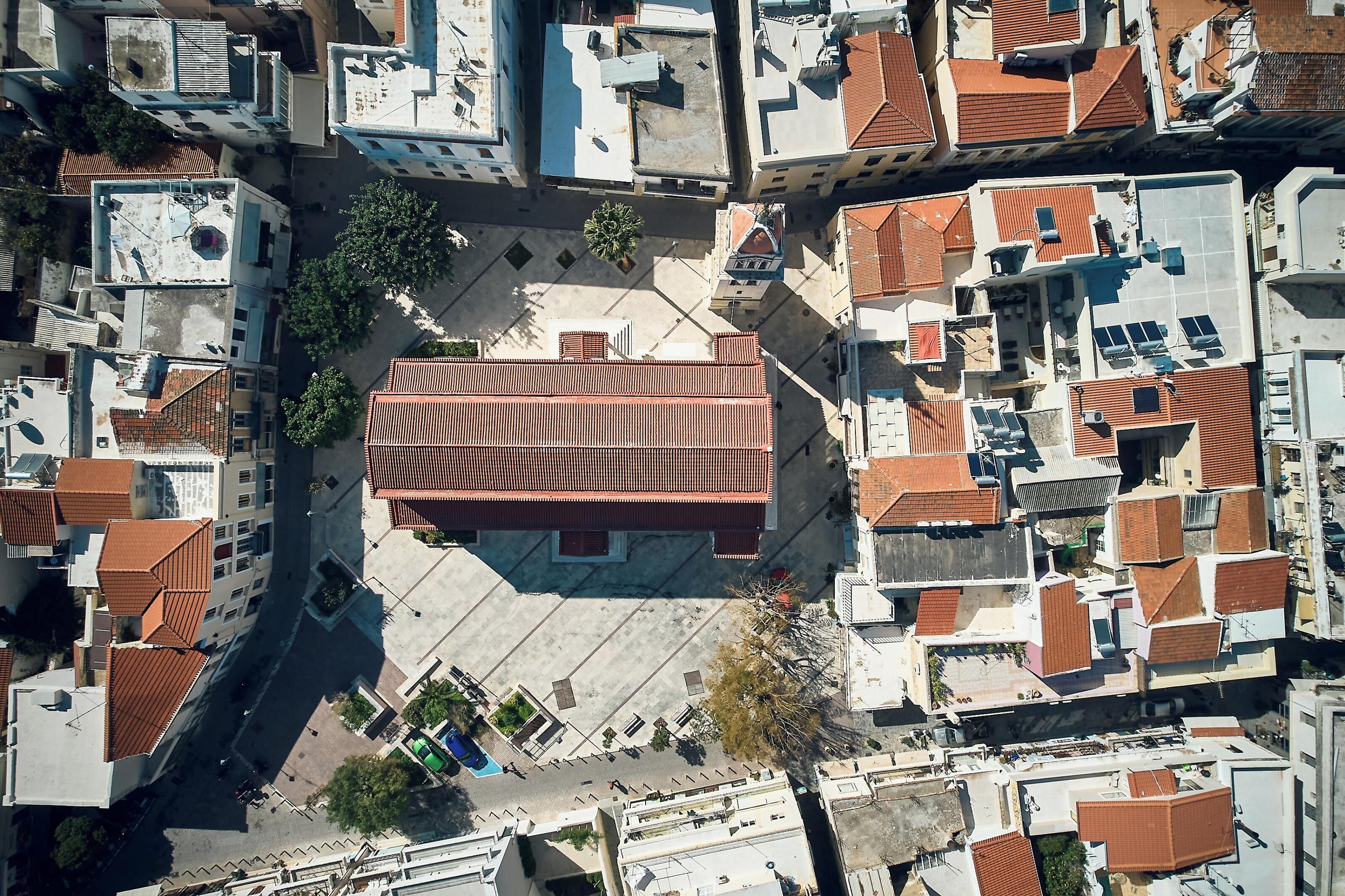 An aerial view of a densely packed urban area with buildings featuring red-tiled roofs and a central open square.