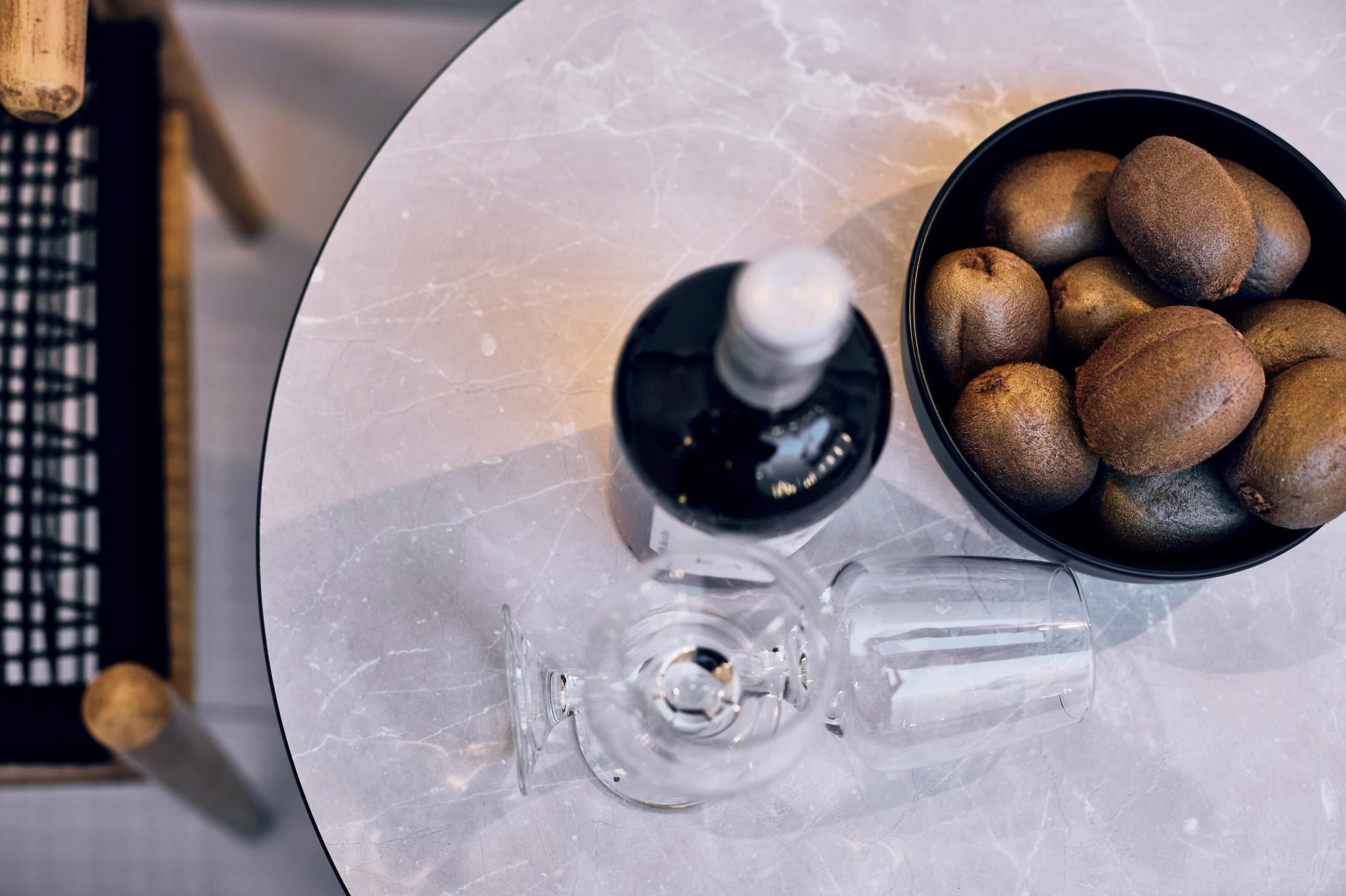 Una mesa con un tazón de kiwis, una botella y una copa de vino.