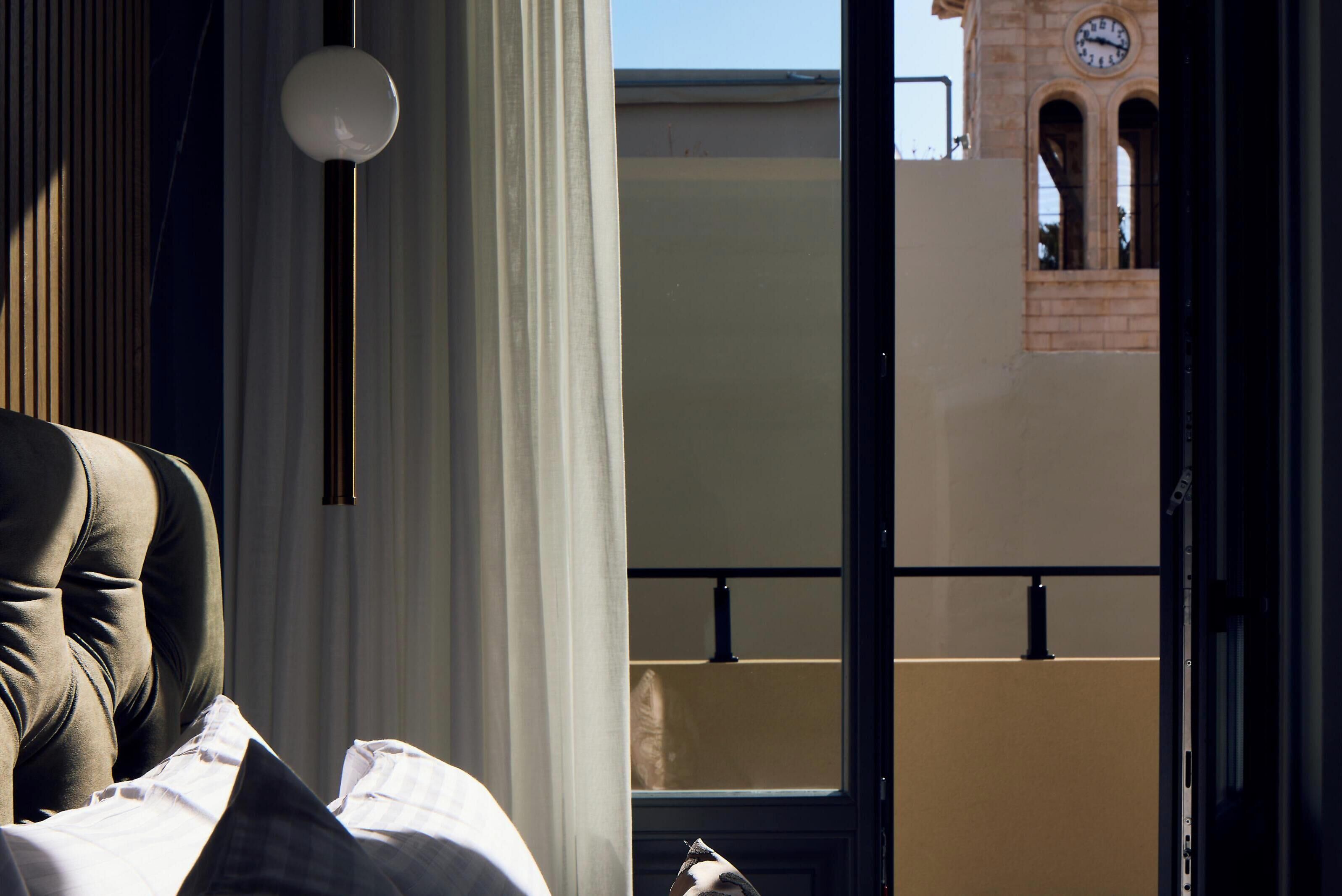 Habitación de hotel con cama, lámpara colgante y vista de un edificio con torre de reloj.