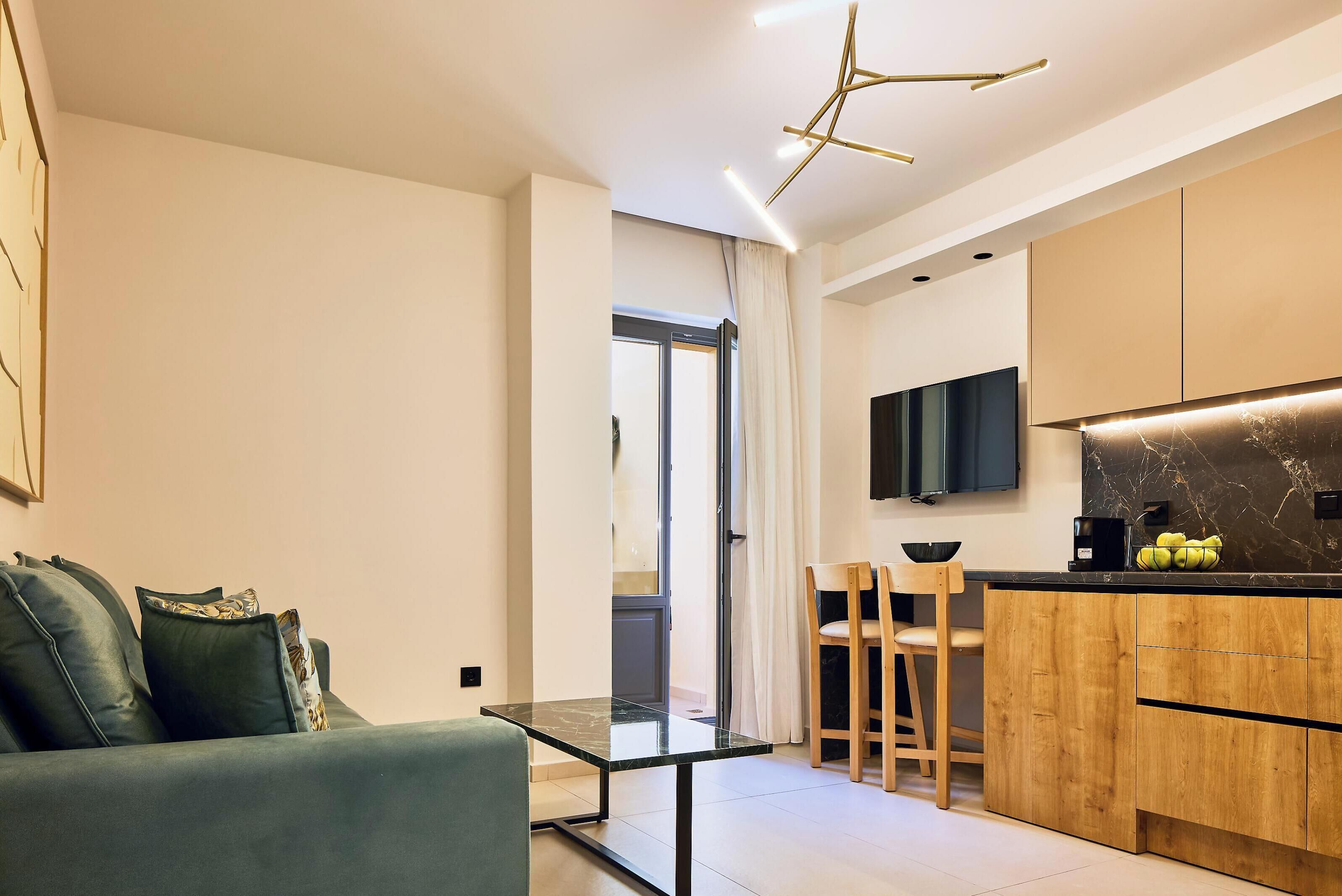 A modern living room with a glass coffee table, a sofa, and a kitchen area with wooden cabinets and a black countertop.