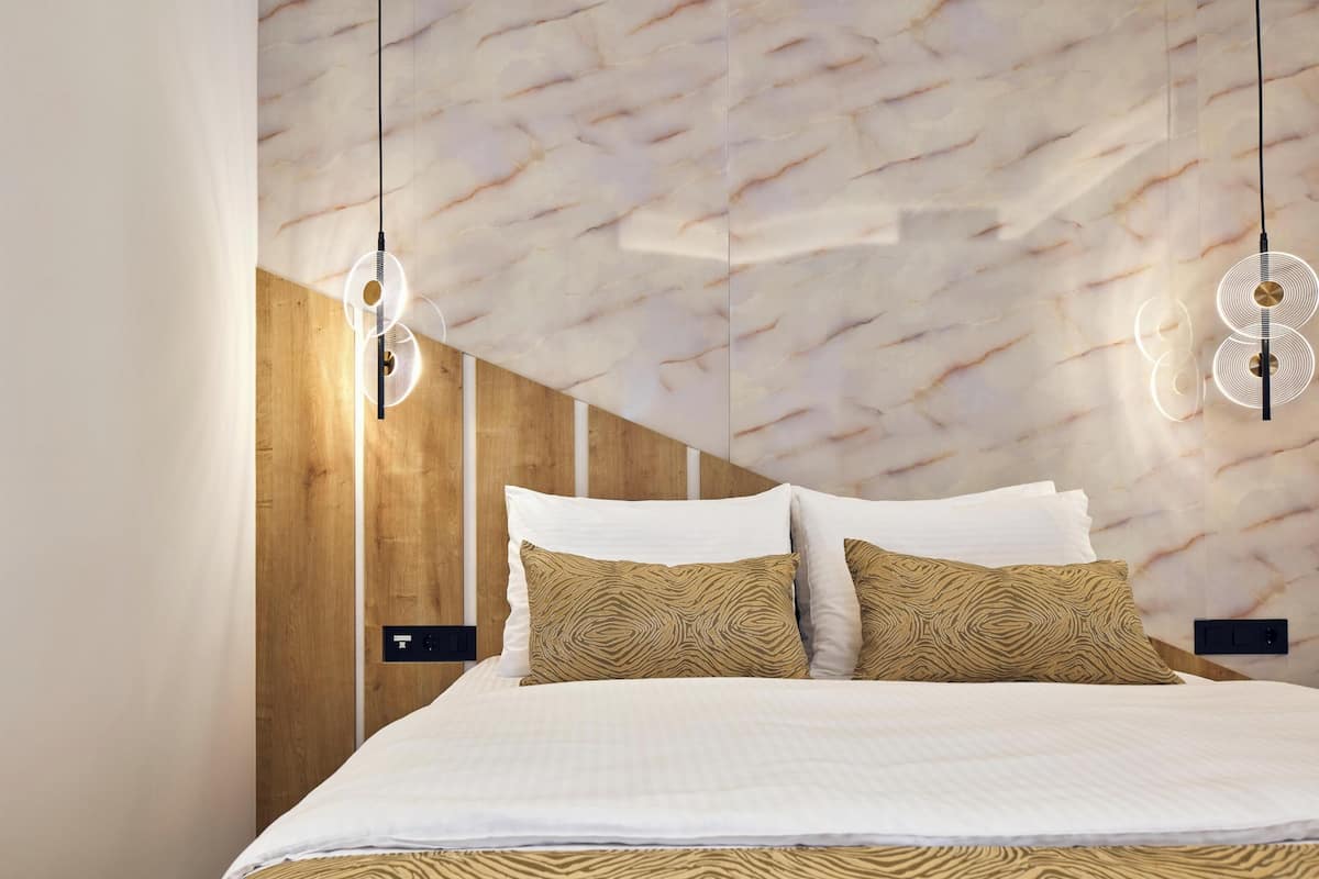 Une chambre moderne avec une tête de lit à motifs de marbre, un mur d’accent en bois et un lit avec une literie blanche et des coussins à motifs.