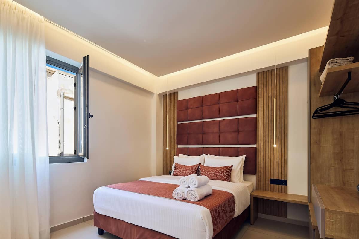 Une chambre d’hôtel moderne avec un grand lit, une tête de lit en bois, une table de chevet et un porte-manteau mural.