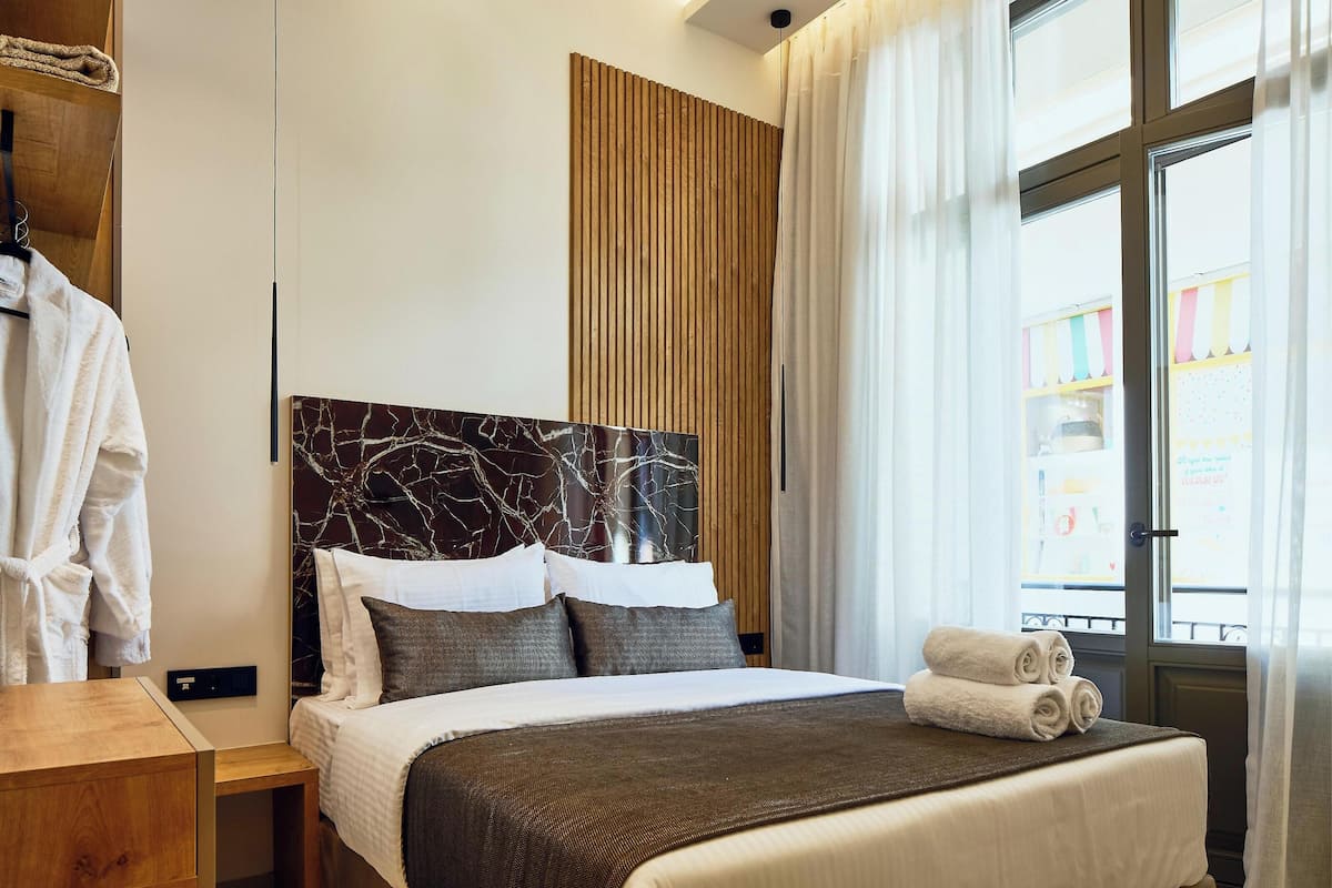 Une chambre d’hôtel avec un lit, une table de chevet en bois, un peignoir et une vue par la fenêtre.