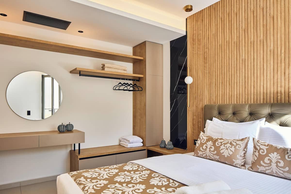 Une chambre à coucher moderne avec un lit, un miroir rond, une coiffeuse en bois et une tête de lit dotée d’un panneau noir.