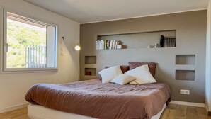 Ein Schlafzimmer mit Bett, Nachttischlampe, Fenster und integrierten Bücherregalen.
