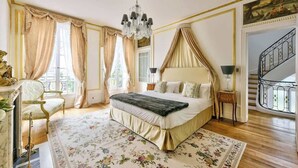 A bedroom with a large bed, a chandelier, curtains, a floral rug, and a staircase in the background. - Parisian Villa: City Views, 5 Bedrooms & Family-Friendly (Paris)