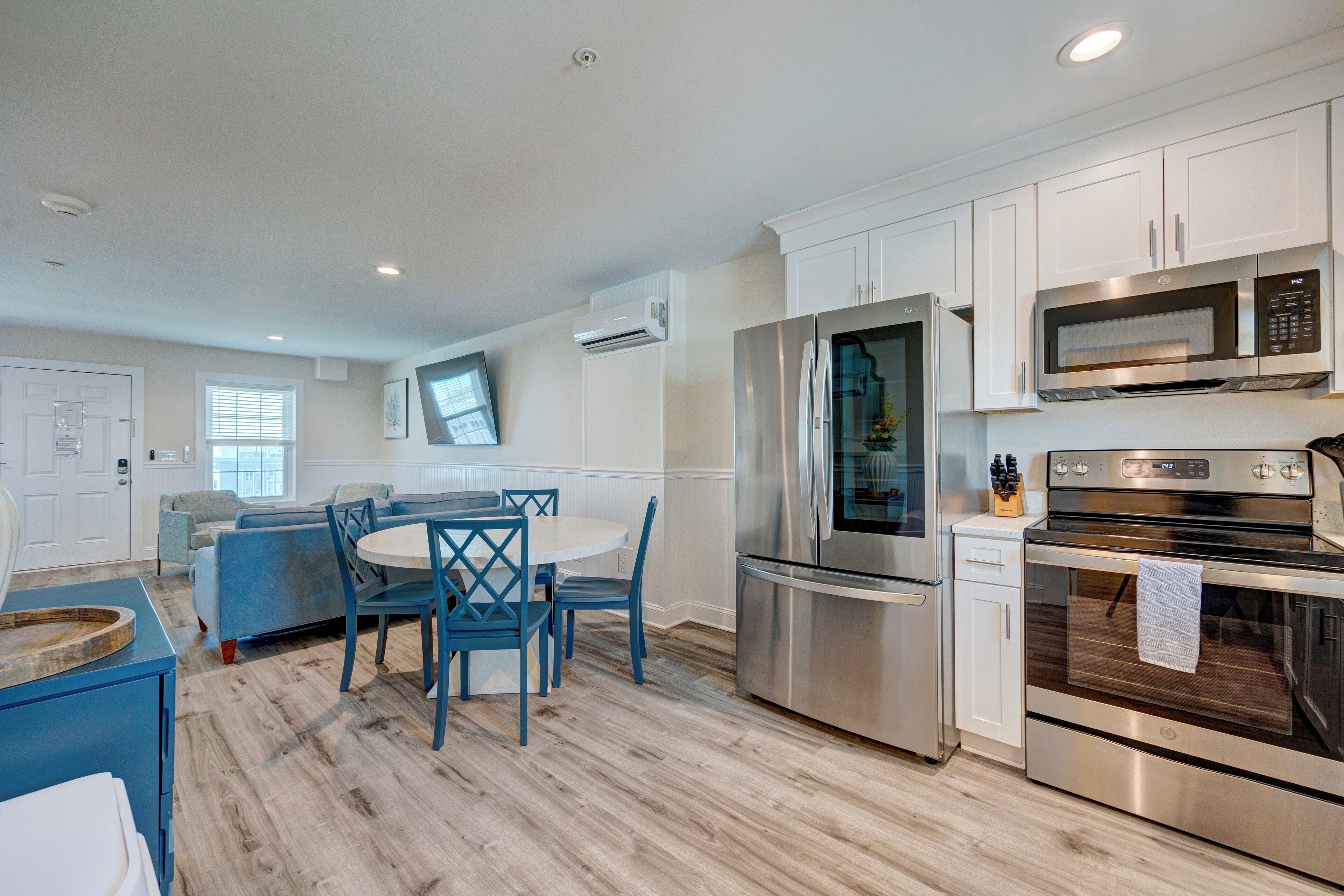 A modern kitchen with white cabinets, stainless steel appliances, and a blue dining area.
